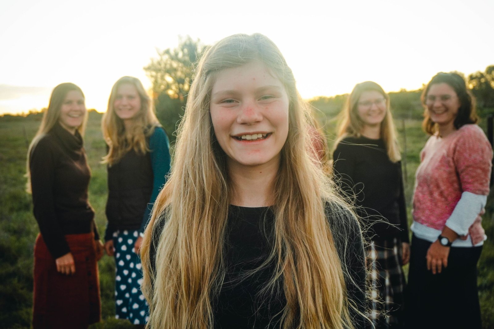 Outdoor group portrait of smiling teenage girl with friends in a field during sunset.